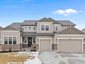 View of front of house with an attached garage, driveway, roof with shingles, and stone siding