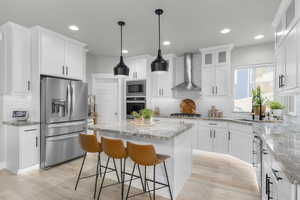 Kitchen with sink, white cabinetry, stainless steel appliances, a kitchen island, and wall chimney exhaust hood