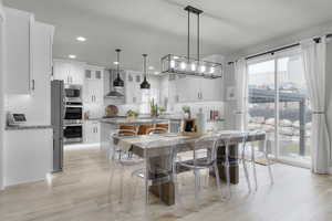 Kitchen with pendant lighting, appliances with stainless steel finishes, light stone countertops, white cabinets, and wall chimney exhaust hood