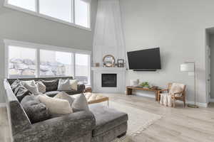 Living room with a towering ceiling, plenty of natural light, a Fireplace, and light hardwood / wood-style flooring