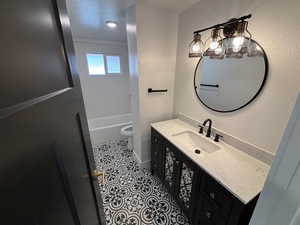 Full bathroom featuring a textured wall, toilet, tile patterned floors, vanity, and shower / washtub combination