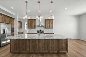 Kitchen featuring wall chimney range hood, a kitchen island with sink, appliances with stainless steel finishes, and a sink