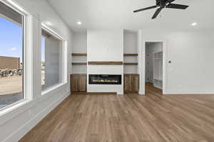 Unfurnished living room featuring light wood finished floors, recessed lighting, a glass covered fireplace, and baseboards