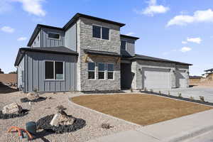 View of front facade with an attached garage, stone siding, a front lawn, and board and batten siding