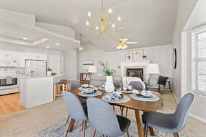 Dining area with ceiling fan with notable chandelier, high vaulted ceiling, a tiled fireplace, and baseboards