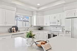 Kitchen with light countertops, white appliances, a raised ceiling, and white cabinetry