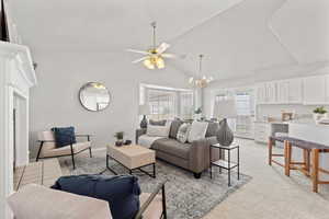 Living room with high vaulted ceiling, light colored carpet, baseboards, and ceiling fan with notable chandelier