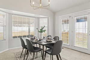 Dining room featuring a chandelier, carpet, lofted ceiling, and baseboards