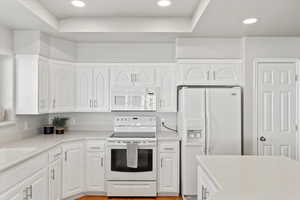 Kitchen featuring light countertops, white appliances, white cabinets, and recessed lighting