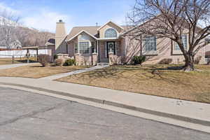 View of front facade with a carport, a front yard, brick siding, and a chimney