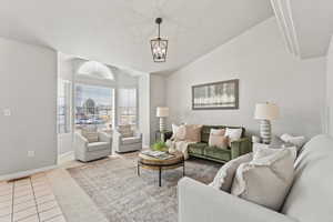 Living area featuring a notable chandelier, light carpet, visible vents, baseboards, and vaulted ceiling