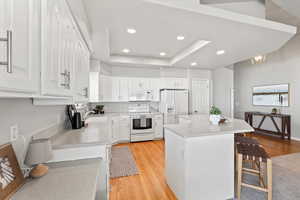 Kitchen with a breakfast bar area, white appliances, white cabinets, light countertops, and a raised ceiling