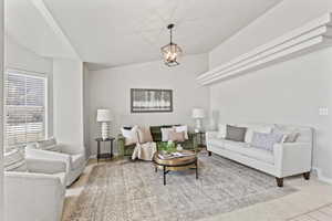 Living room featuring vaulted ceiling, light carpet, a chandelier, and baseboards