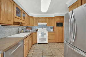 Kitchen with stainless steel appliances, light countertops, glass insert cabinets, a sink, and under cabinet range hood