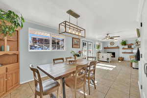 Dining space with a warm lit fireplace, light tile patterned floors, baseboards, a ceiling fan, and crown molding