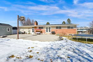 Snow covered rear of property featuring a trampoline, brick siding, a patio, a chimney, and a hot tub