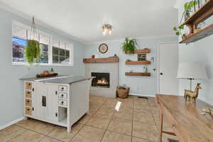 Interior space with light tile patterned floors, a fireplace, baseboards, and crown molding