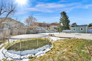 Yard covered in snow featuring an outbuilding, a storage unit, a trampoline, and fence