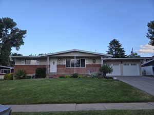 View of front facade featuring concrete driveway, an attached garage, covered porch, a front lawn, and brick siding