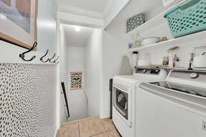 Clothes washing area featuring ornamental molding, laundry area, separate washer and dryer, and light tile patterned floors