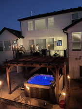 Back of house at night featuring an outdoor hot tub, a deck, and stucco siding