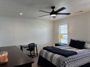 Bedroom with a ceiling fan, visible vents, and a textured ceiling