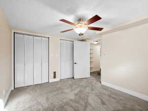 Unfurnished bedroom with a textured ceiling, light colored carpet, a ceiling fan, baseboards, and multiple closets