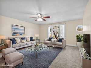 Carpeted living room featuring a ceiling fan and baseboards