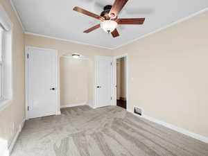 Unfurnished bedroom featuring arched walkways, light colored carpet, visible vents, baseboards, and crown molding