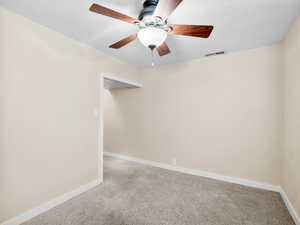 Empty room with a ceiling fan, light colored carpet, visible vents, and baseboards