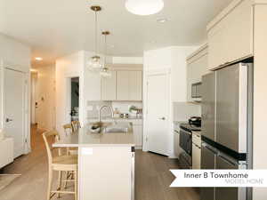 Kitchen featuring stainless steel appliances, light countertops, hanging light fixtures, a kitchen island with sink, and a sink