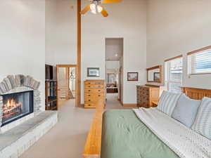 Bedroom featuring a high ceiling, baseboards, a stone fireplace, and light colored carpet