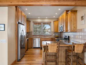 Kitchen with appliances with stainless steel finishes, a sink, light wood-type flooring, a peninsula, and a kitchen breakfast bar