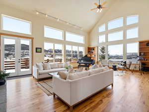 Living room with light wood-style flooring, rail lighting, high vaulted ceiling, french doors, and a mountain view