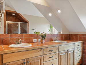 Bathroom featuring double vanity, vaulted ceiling, and a sink