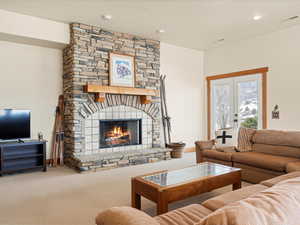 Living room featuring a stone fireplace, recessed lighting, carpet flooring, visible vents, and french doors