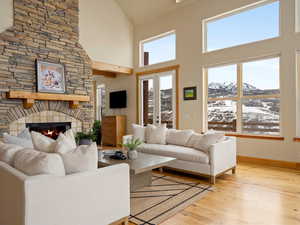 Living room featuring high vaulted ceiling, a stone fireplace, light wood-style flooring, and baseboards