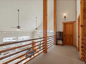 Corridor featuring high vaulted ceiling, light colored carpet, and track lighting