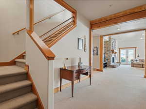 Stairs featuring beam ceiling, french doors, carpet flooring, a stone fireplace, and baseboards