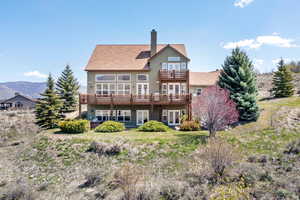 Rear view of house featuring a chimney, stucco siding, a deck with mountain view, french doors, and a balcony