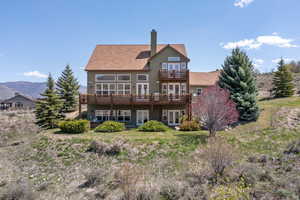 Back of property featuring a balcony, a chimney, stucco siding, a deck with mountain view, and french doors