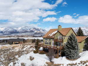 Snow covered back of property featuring a deck with mountain view, a chimney, and stucco siding