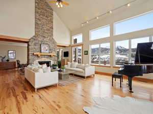 Living area with light wood finished floors, baseboards, a ceiling fan, a fireplace, and high vaulted ceiling