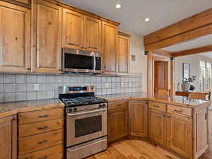 Kitchen with appliances with stainless steel finishes, brown cabinetry, light wood-style flooring, and a peninsula