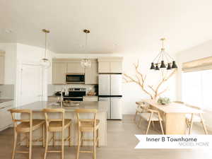 Kitchen with a breakfast bar, stainless steel appliances, backsplash, light wood-style floors, and an island with sink