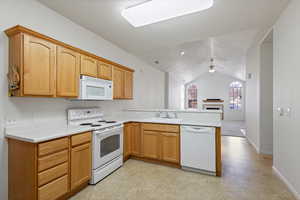 Kitchen with white appliances, ceiling fan, a peninsula, light countertops, and a sink