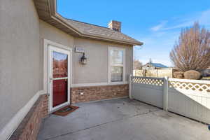 Entrance to property with a shingled roof, a chimney, fence, a patio area, and stucco siding