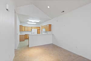 Kitchen with white appliances, visible vents, a peninsula, vaulted ceiling, and light countertops.  The refrigerator stays.