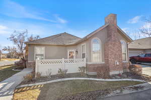 View of front of home with brick siding, a shingled roof, fence, and stucco siding