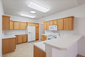 Kitchen featuring white appliances, light countertops, a peninsula, and light floors